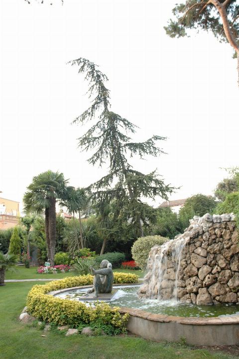 Font amb cascada i escultura envoltada de gespa i palmeres, en format vertical